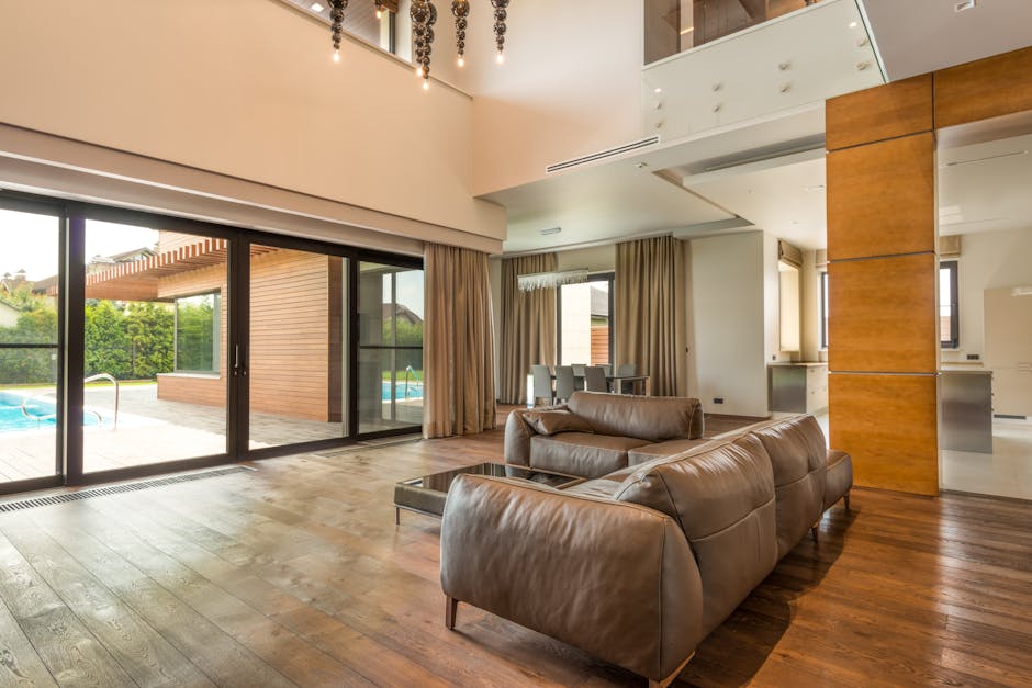 Spacious and modern living room with pool view, featuring sofas and wooden flooring.