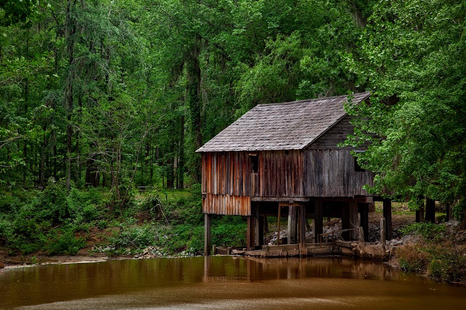 A scenic view of a rustic water mill surrounded by lush greenery at daytime.